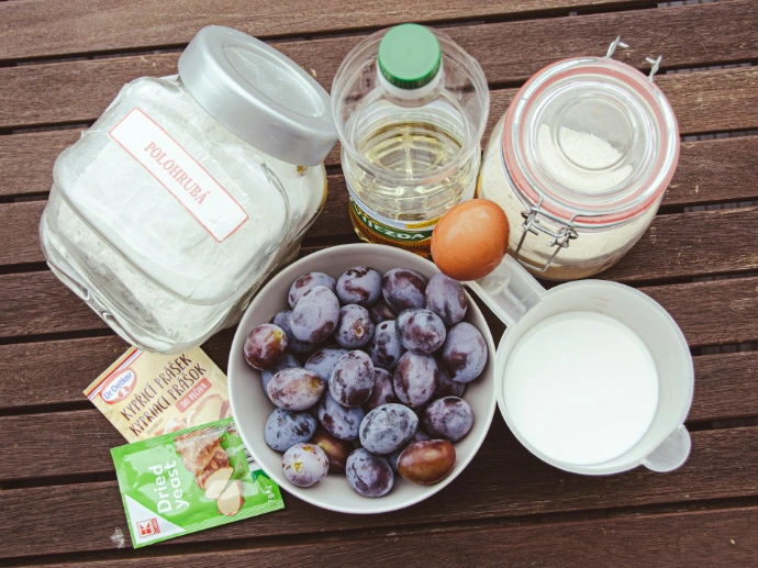 a bowl of plums, eggs, milk, and other ingredients on a table